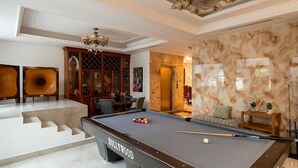 Une chambre luxueuse dotée d’une table de billard, d’un lustre, de murs en marbre et d’un escalier.