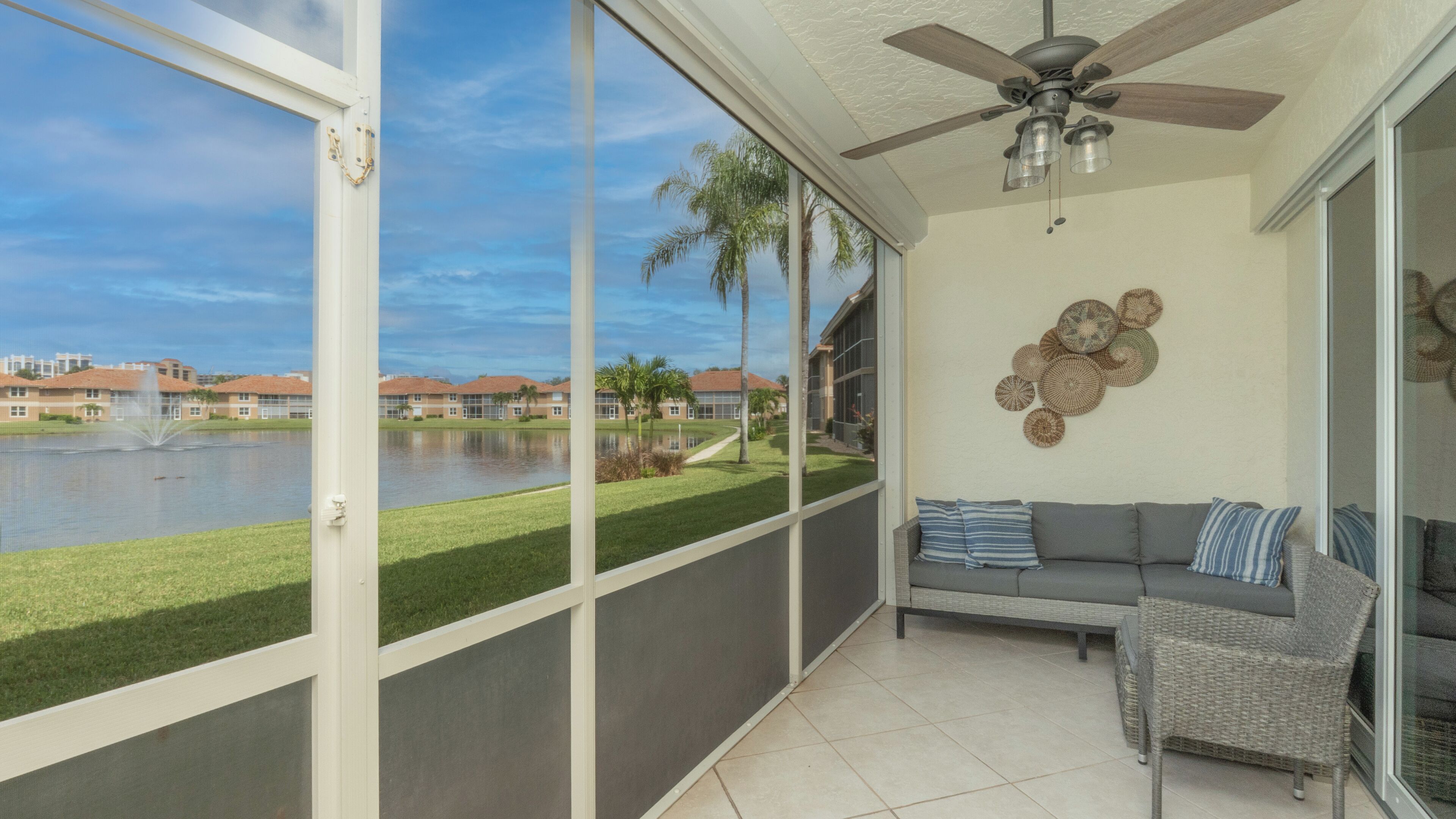 A balcony with a view of a lake, a ceiling fan, and a seating area with cushions.