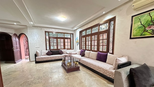 A spacious living room with a large sectional sofa, a coffee table, and a large window with decorative glass panes. - residence riad zitoune (Marrakech)