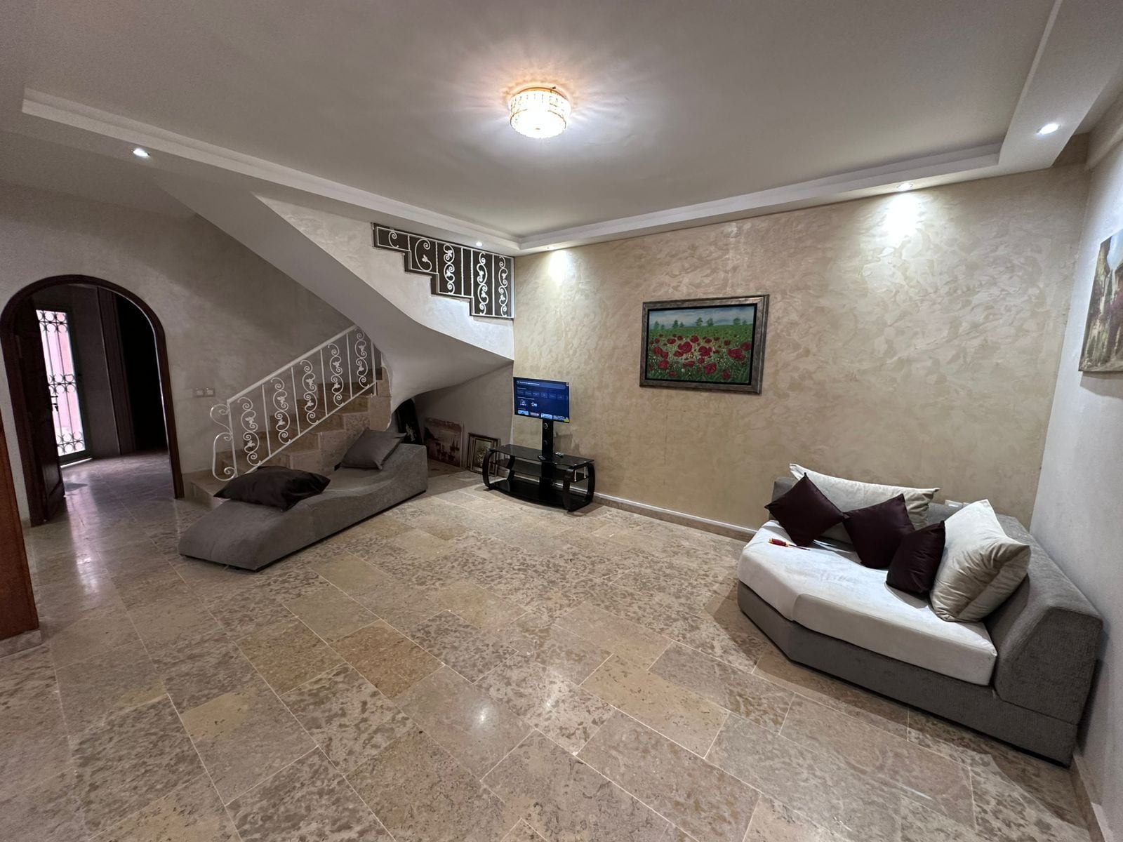 A spacious living area with a high ceiling, a staircase, a flat-screen TV, and a painting on the wall.