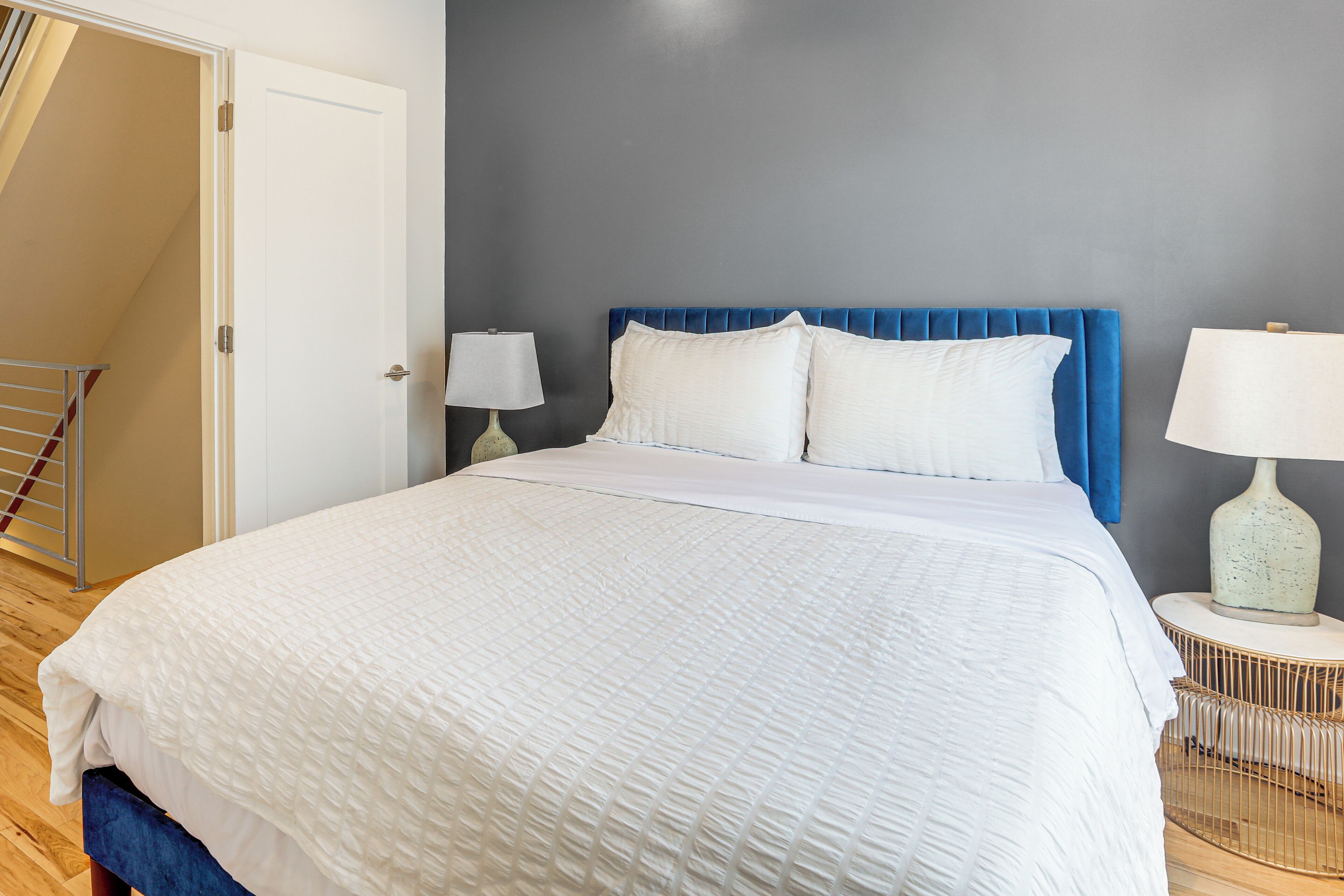 A bedroom with a large bed, two bedside lamps, a blue headboard, and a door to a balcony.