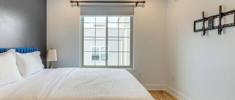 A bedroom with a bed, a window, a wall-mounted TV, and a ceiling fan.