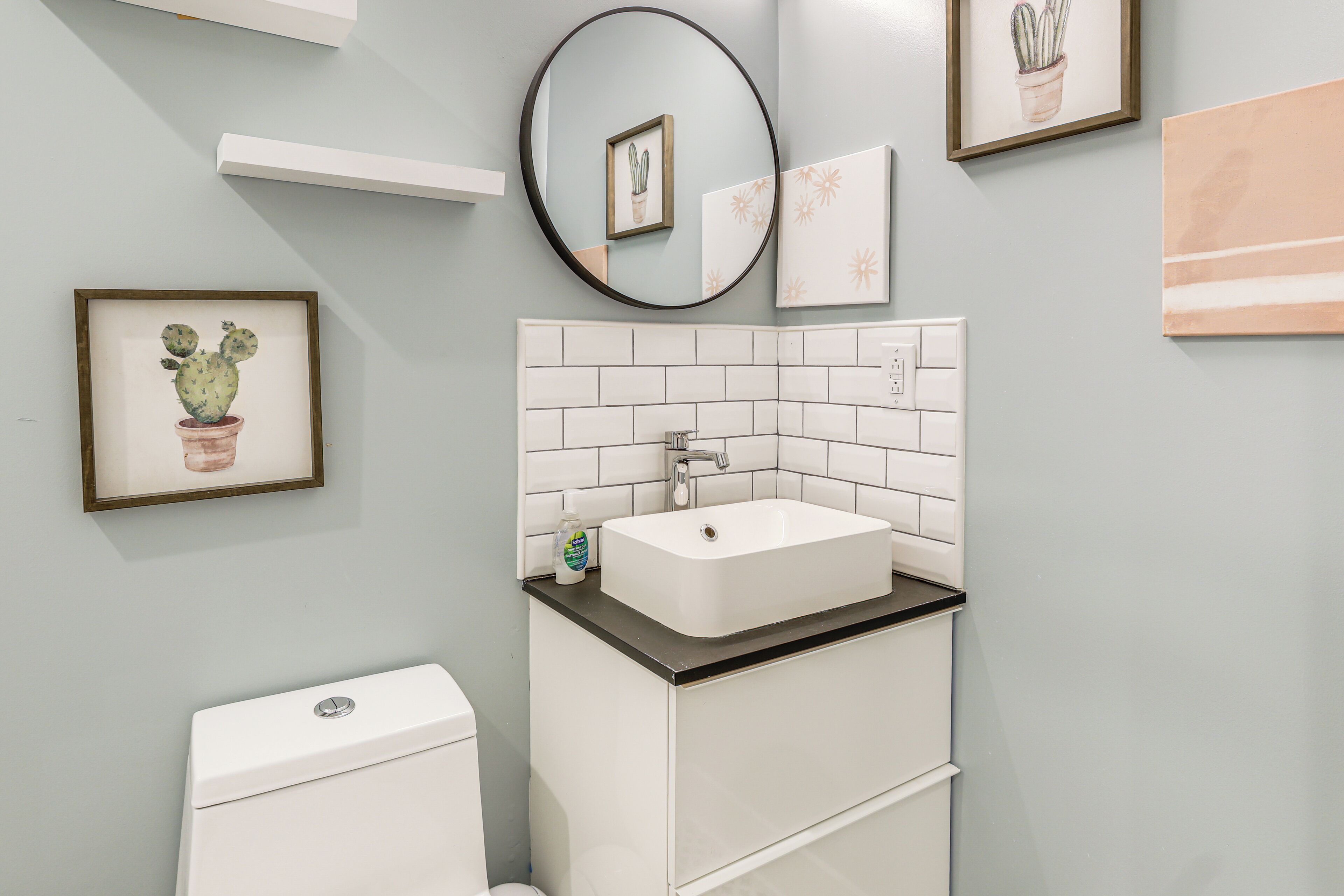 Un bagno con un lavandino bianco, un water, uno specchio e opere d'arte appese alla parete.