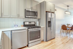 A modern kitchen with stainless steel appliances, a built-in oven, microwave, and refrigerator, and a dining area with wooden chairs and a table. - Philly Hub Near University City, Lincoln Financial (Philadelphia)