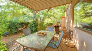 Patio esterno con tavolo in vetro, sedie e barbecue.