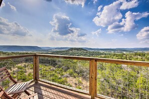 Eine Holzterrasse mit Metallgeländer, die einen Blick auf eine Landschaft mit Bäumen und ferne Hügel bietet.