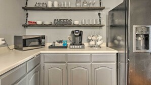 Eine Küche mit Mikrowelle, Kaffeemaschine und Regalen mit Tassen und Gläsern.