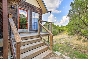 Eine Holzhütte mit einer Holztreppe, die zu einer Glasdoor führt, eingebettet in eine natürliche Landschaft.