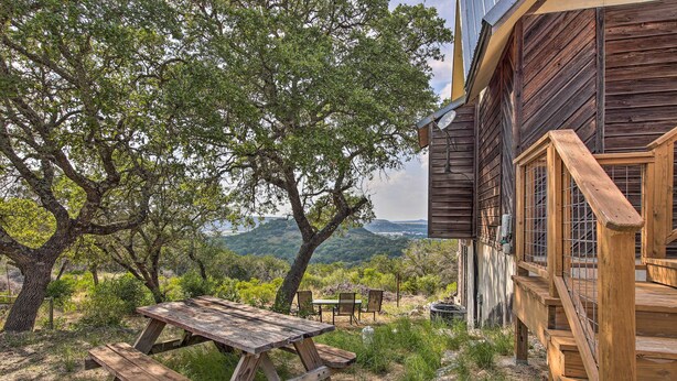 Ein rustikales Holzhaus mit Picknicktisch und Stühlen, umgeben von Bäumen und einer schönen Aussicht.