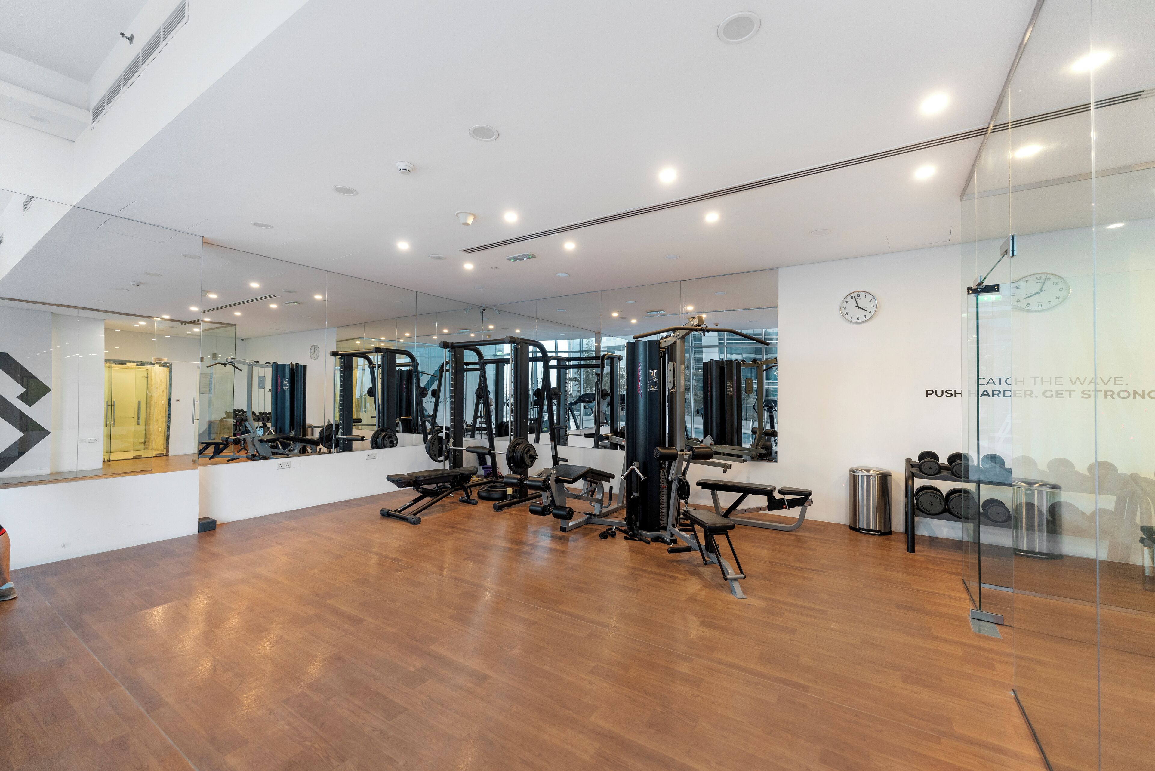 A modern gym with various exercise equipment, large mirrors, and a wooden floor.
