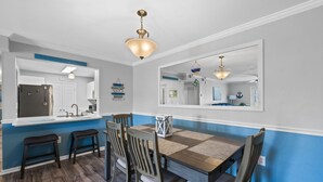 A dining area with a wooden table, four chairs, a chandelier, and a large mirror. - Colony Club E1 (Gulf Shores)