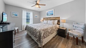 A bedroom with a bed, a desk, a chair, a ceiling fan, and artwork on the walls. - Colony Club E1 (Gulf Shores)