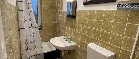 A small bathroom with a shower, sink, toilet, and a welcome sign.