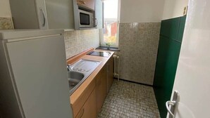 Een kleine keuken met een magnetron, spoelbak en een raam.