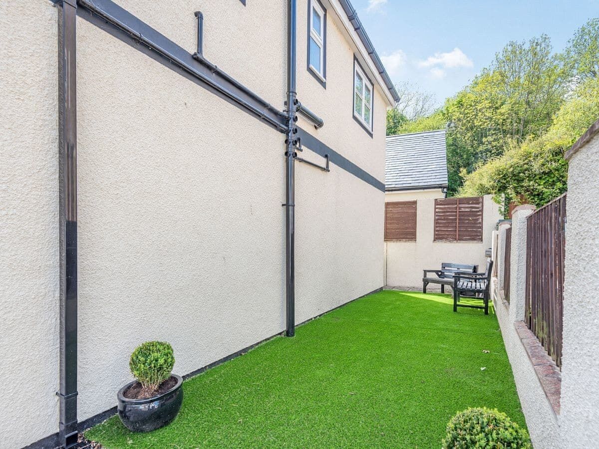 A small, enclosed backyard with artificial grass, a potted plant, and a bench.