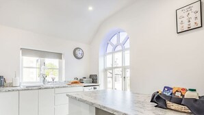 Une cuisine moderne avec des meubles blancs, un plan de travail en marbre et une grande fenêtre.