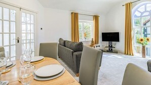 Un coin repas avec une table en bois dressée pour quatre personnes, un canapé et un téléviseur en arrière-plan.