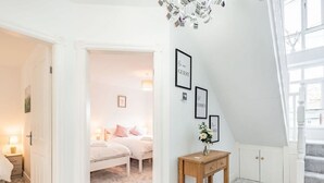 Une chambre à coucher avec un lit, une table de chevet et un petit bureau avec une chaise. Un escalier mène à un étage supérieur.