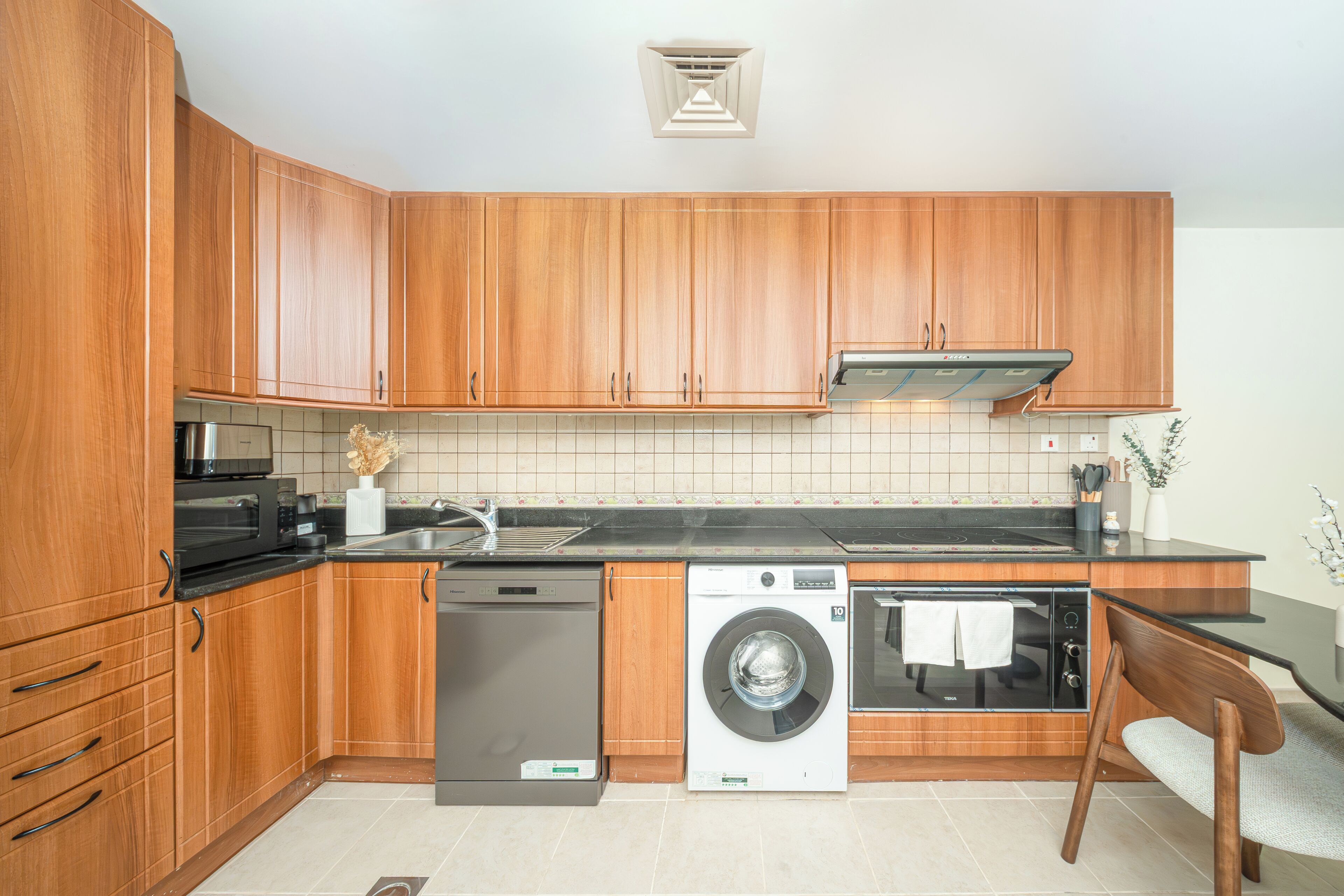 A modern kitchen with wooden cabinets, a dishwasher, a washing machine, and a microwave.