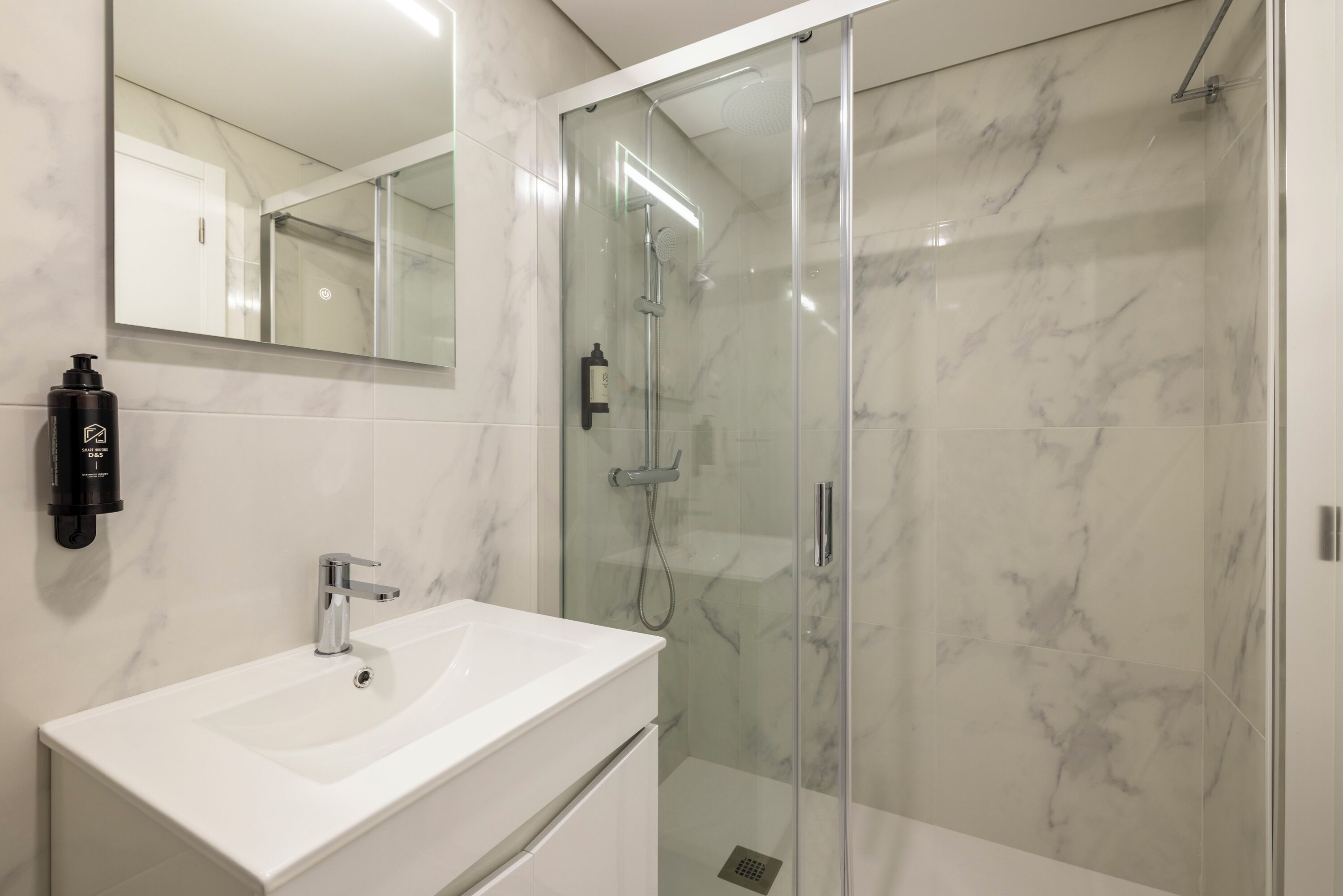 A modern bathroom with a glass-enclosed shower, a white sink, and a large mirror.