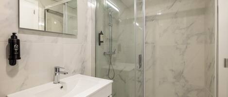 A modern bathroom with a glass-enclosed shower, a white sink, and a large mirror.