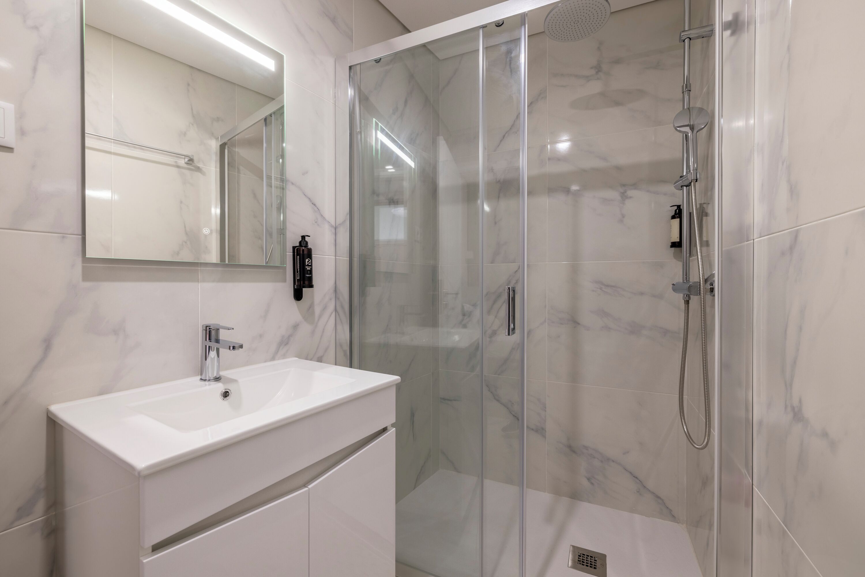 Ein modernes Badezimmer mit einer Glasdusche, einem weißen Waschbecken und einem großen Spiegel.