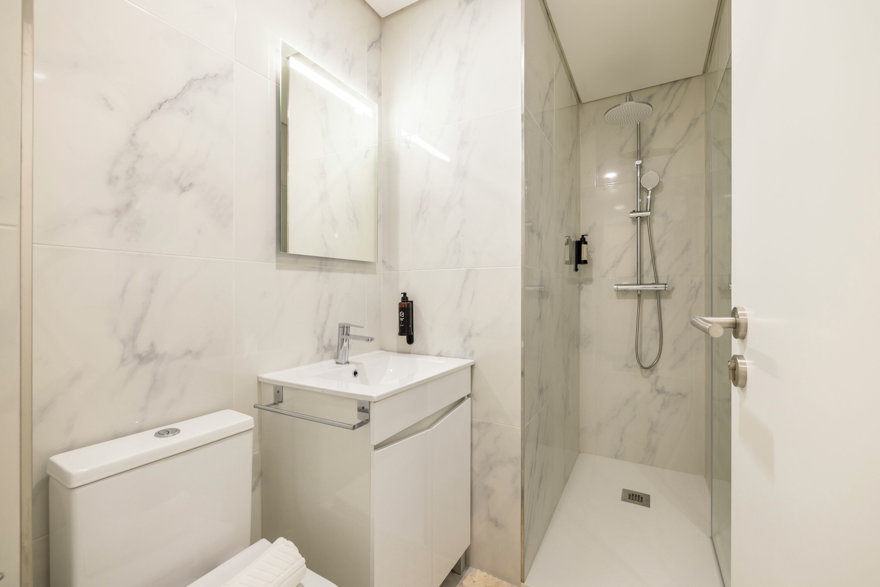 A modern bathroom with a white marble sink, a toilet, and a glass-enclosed shower area.