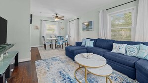 Ein Wohnzimmer mit einem blauen Sofa, einem runden Couchtisch und einem Essbereich mit weißem Tisch und Stühlen.