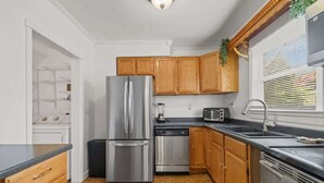 Eine Küche mit Holzschränken, einem Edelstahl-Kühlschrank, einer Spülmaschine, einer Mikrowelle und einem Waschbecken.