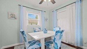 Ein Essbereich mit einem weißen Tisch und Stühlen, einem Deckenventilator und hellblauen Vorhängen.