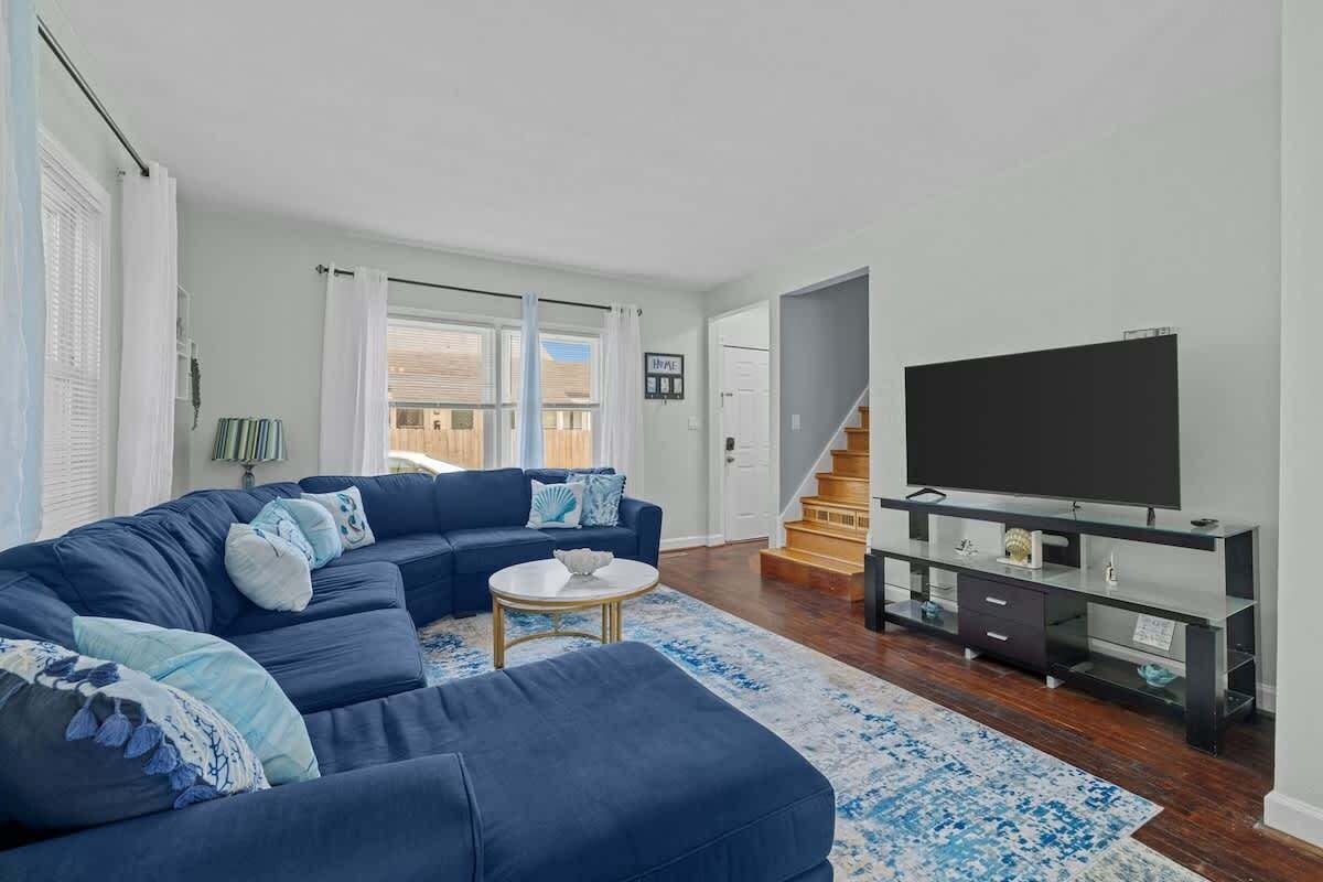 A modern living room with a blue sectional sofa, a flat-screen TV, and a staircase leading to another level.