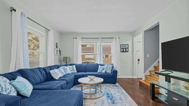 Ein modernes Wohnzimmer mit einem blauen Ecksofa, einem runden Couchtisch und einer TV-Konsole aus Glas.