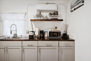 A kitchen with a wooden countertop, white cabinets, a coffee maker, a microwave, and a shelf with dishes.