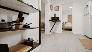 Une petite cuisine équipée d’une étagère en bois, d’une cuisinière et d’un four à micro-ondes. On aperçoit un lit dans la pièce adjacente.