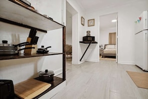 A compact kitchen with a wooden shelf, a stove, and a microwave. A bed is visible in the adjacent room.