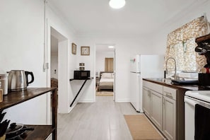 A compact kitchen with a microwave, kettle, and sink. A bed is visible in the adjacent room.