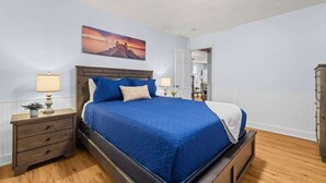 Een slaapkamer met een bed, nachtkastjes, een lamp, een schilderij en een garderobe.