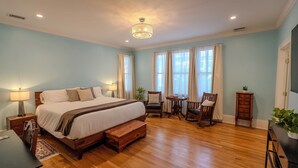 A spacious bedroom with a large bed, wooden floor, and a chandelier. - 7BR/10BA Five Points Private Gathering Home | Sleeps 26, Theatre, Golf Sim, Elevator & Outdoor Areas (Raleigh)