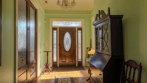 A hallway with a wooden door, a chandelier, and a cabinet. - 7BR/10BA Five Points Private Gathering Home | Sleeps 26, Theatre, Golf Sim, Elevator & Outdoor Areas (Raleigh)