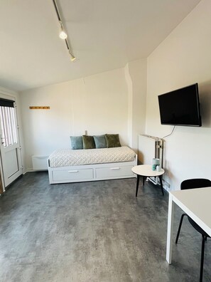 A modern bedroom with a bed, bedside table, and a mounted TV. - Cozy studio 500 m from the ferry and city center - perfect for 2 people (Hirtshals)