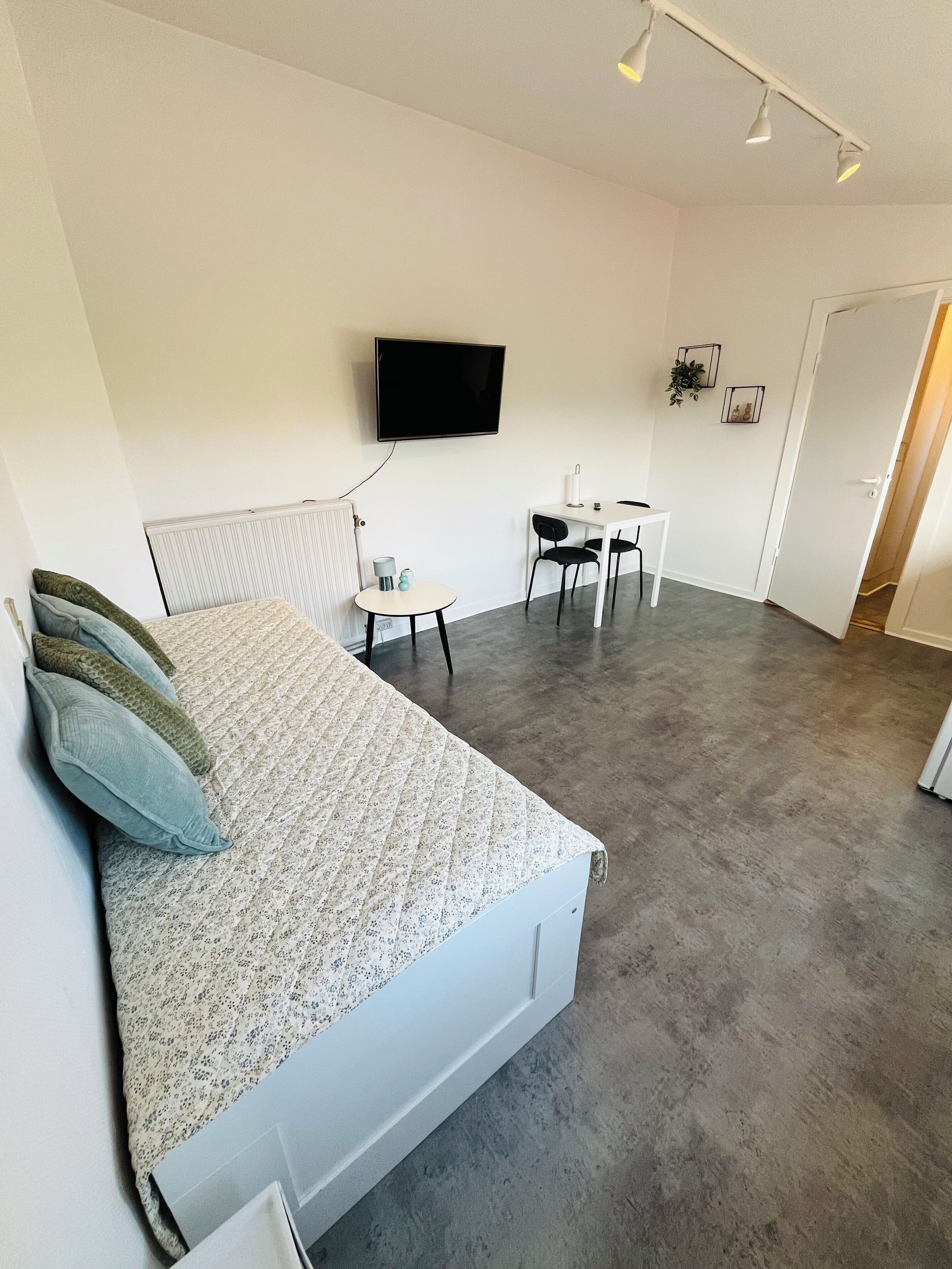 A modern bedroom with a bed, a desk, and a television.