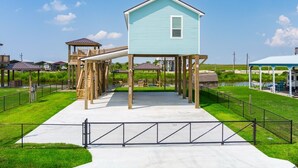 A waterfront property with a light blue house, wooden deck, and a covered area. - Mabry 1 Bedroom Home (Port Bolivar)