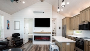 A modern kitchen with white cabinetry, a built-in stove, and a large flat-screen TV. - Mabry 1 Bedroom Home (Port Bolivar)