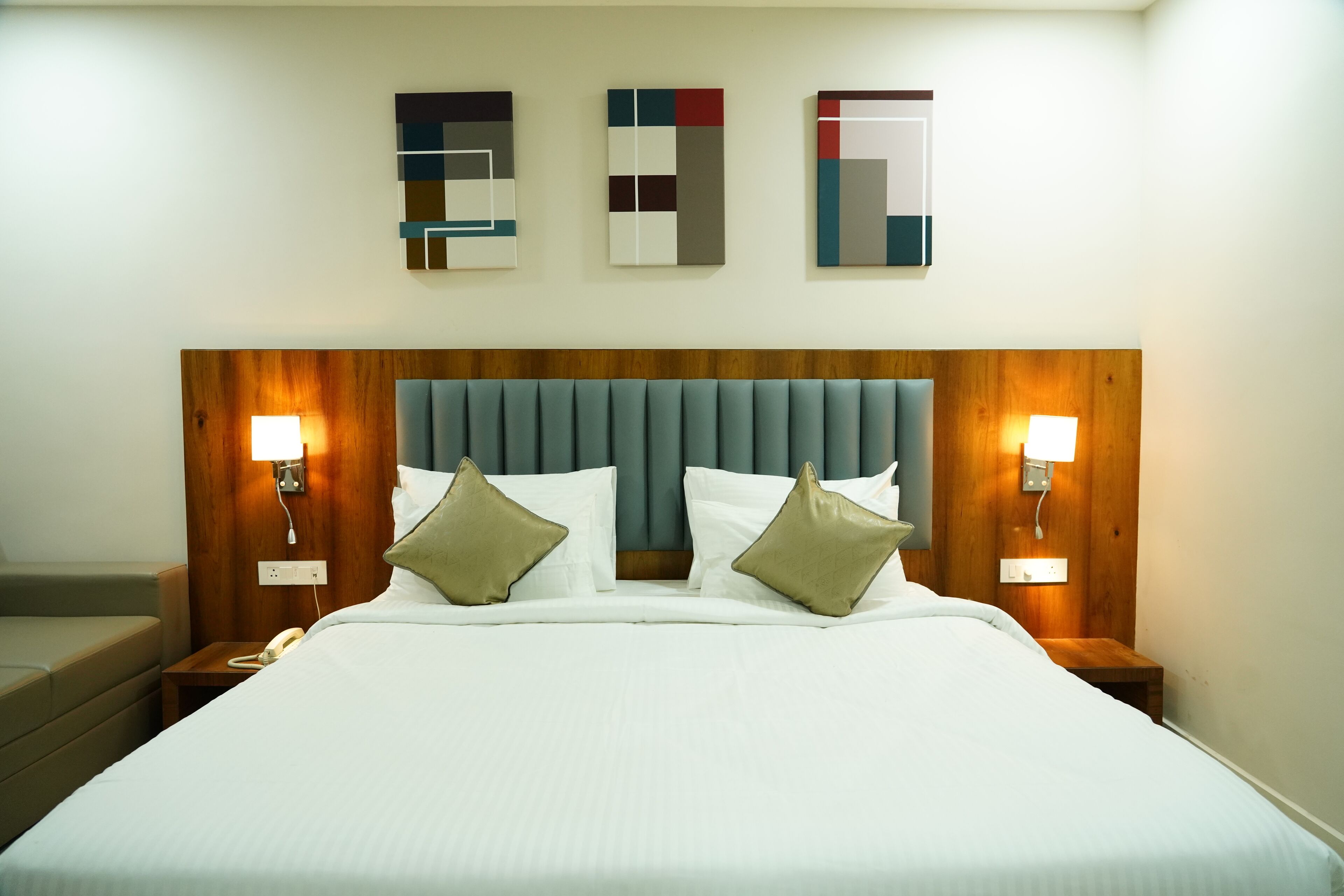 A hotel room with a large bed, two bedside tables, a wooden headboard, and three wall-mounted artworks.