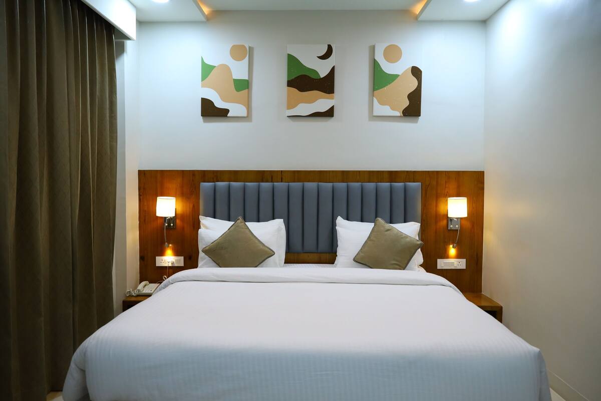 A hotel room with a large bed, two bedside tables with lamps, a wooden headboard, and three abstract wall art pieces.