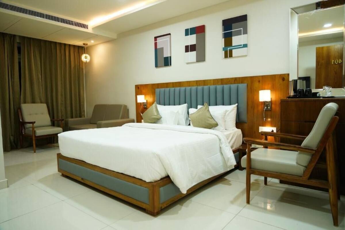 A hotel room with a large bed, two armchairs, a desk, and a mirror.