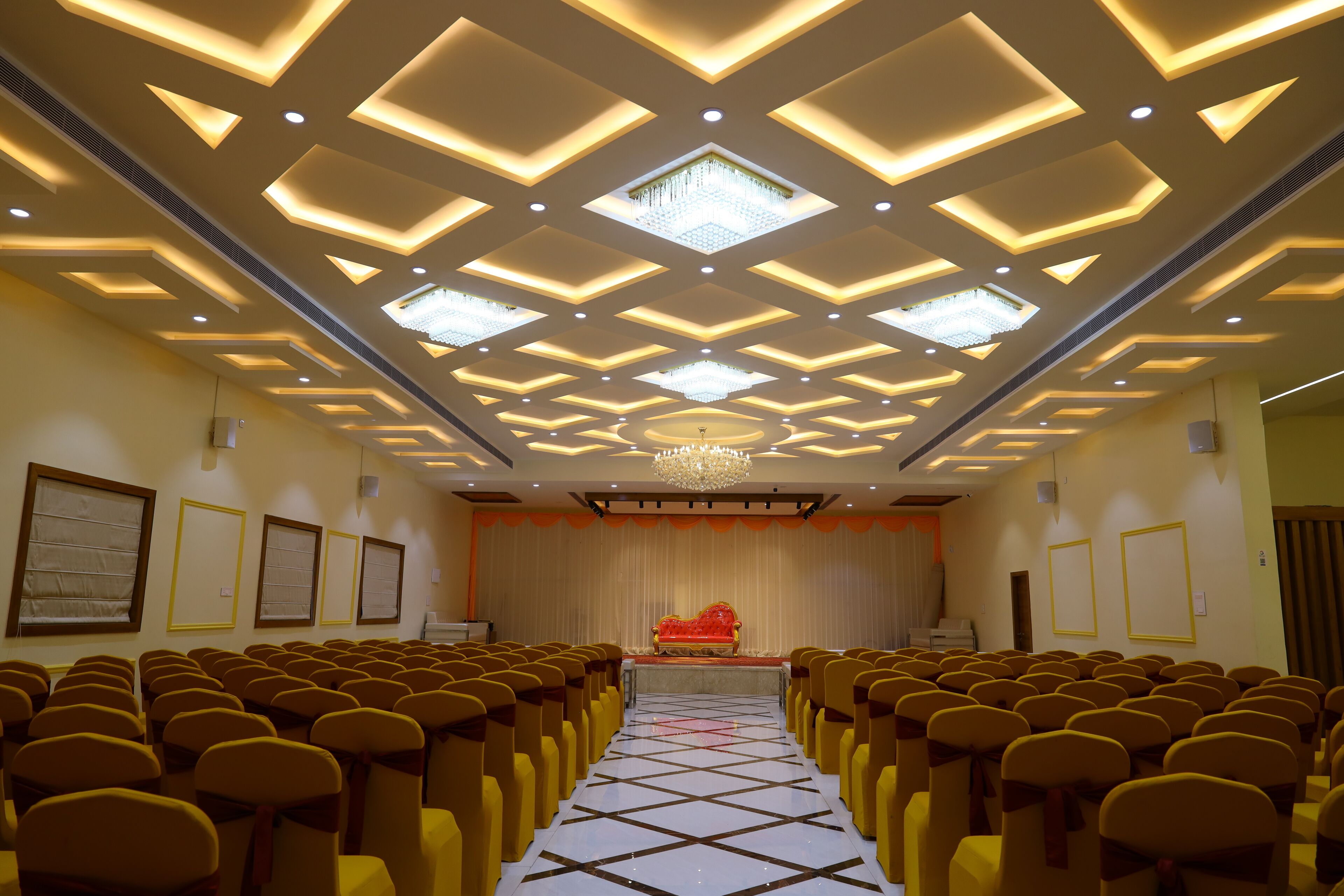 A conference room with rows of chairs, a stage with a red sofa, and a chandelier.