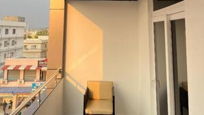 A balcony with a wooden ceiling, a chair, and a view of a building with a sign. - Hotel Pasupala Inn (Anantapur)