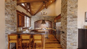 A kitchen with stone walls, wooden bar stools, and a central island. - Cozy Cabin by InvitedHome | Theater Room, Bunk Room, Vaulted Ceilings (Mountain Village)