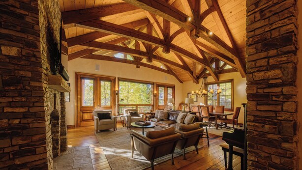 A spacious living room with a high wooden ceiling, stone walls, and large windows allowing natural light. - Cozy Cabin by InvitedHome | Theater Room, Bunk Room, Vaulted Ceilings (Mountain Village)